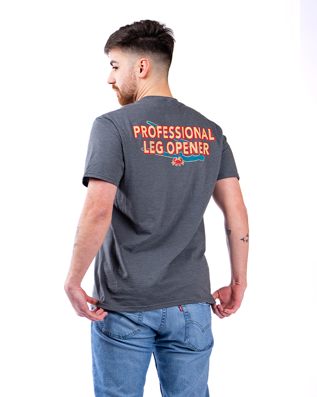The image shows a person from the back, wearing a grey t-shirt with red and white text. Printed in bold, capital letters across the upper back of the shirt is the phrase “PROFESSIONAL LEG OPENER.” Below the text, there is a small graphic of a red crab. The individual is also wearing blue jeans and is standing against a white background.