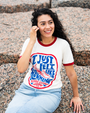 A person with curly hair sits on rocky terrain, wearing a vintage T-shirt with the text "I Just Felt Like Running" and blue jeans.