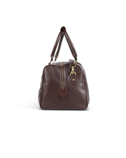 Side view of brief case. A brown leather duffel bag with a textured surface is centered against a white background. The bag features two rolled handles attached with brass-colored metal hardware, a detachable shoulder strap, and a zipper closure on top.