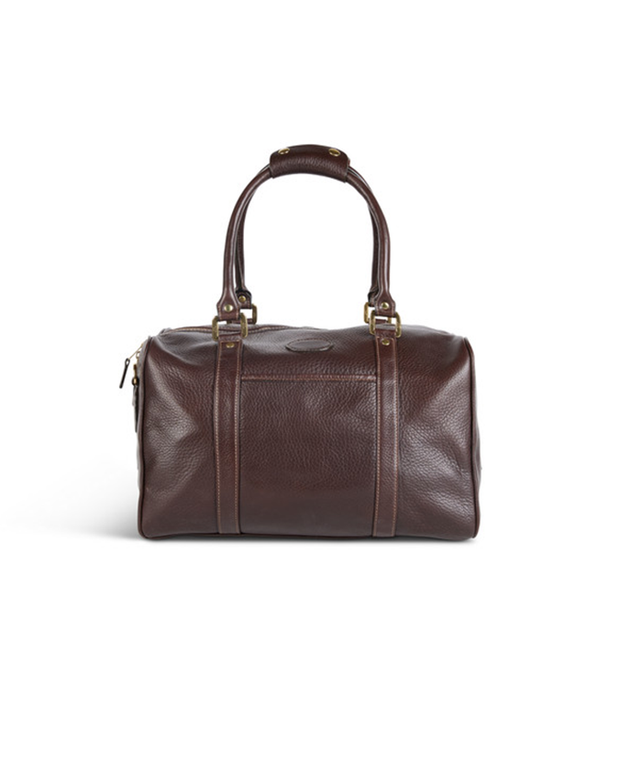 A brown leather duffel bag with a textured surface is centered against a white background. The bag features two rolled handles attached with brass-colored metal hardware, a detachable shoulder strap, and a zipper closure on top.