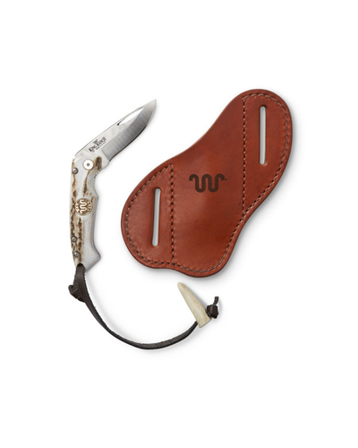 A folding knife with a decorative handle next to a brown leather sheath. The handle appears to have bone or ivory inlays and is etched with designs, while the sheath has a stamped King Ranch logo on a white background.