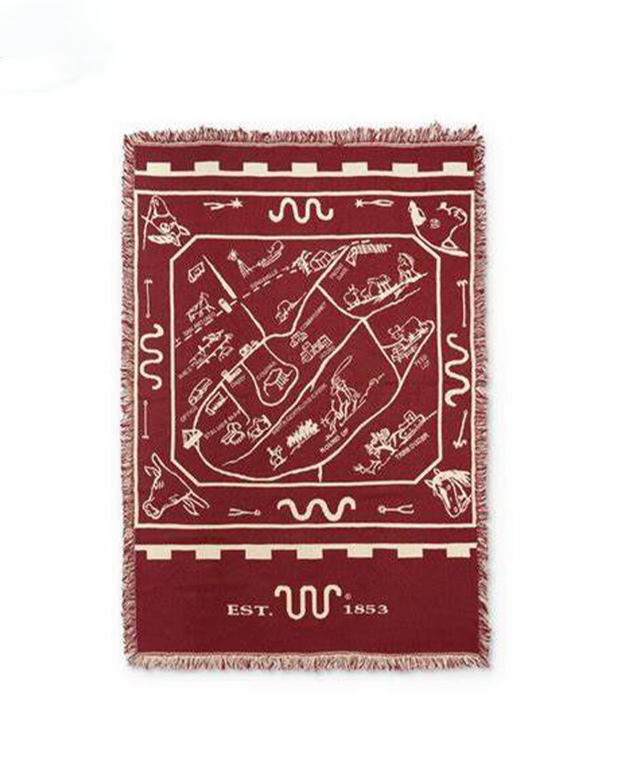 Rectangular throw blanket with fringed edges. The blanket features a maroon and white color scheme and a central design that includes various cattle, horses and cowboys-themed graphics. King Ranch icon logo with the text 'EST. 1853' at the bottom.