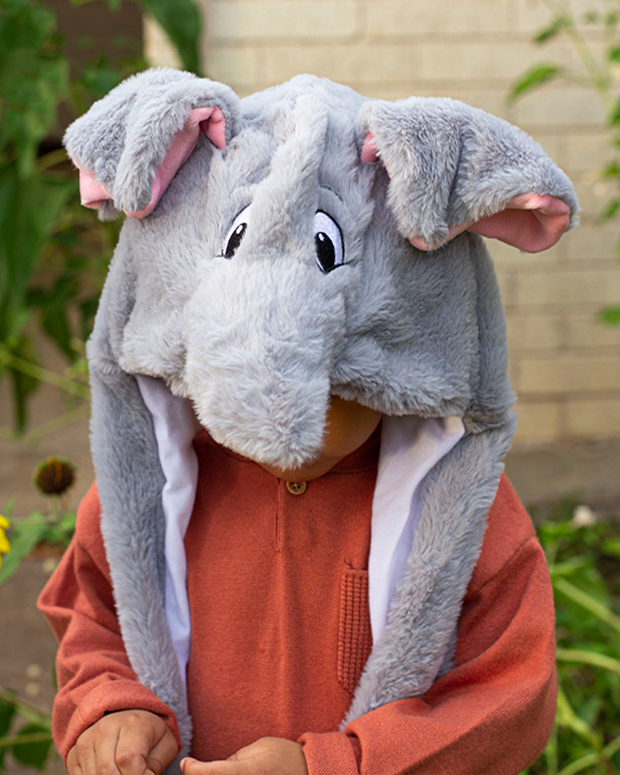 Small child wearing grey Tuki the Elephant plush hat while standing outside