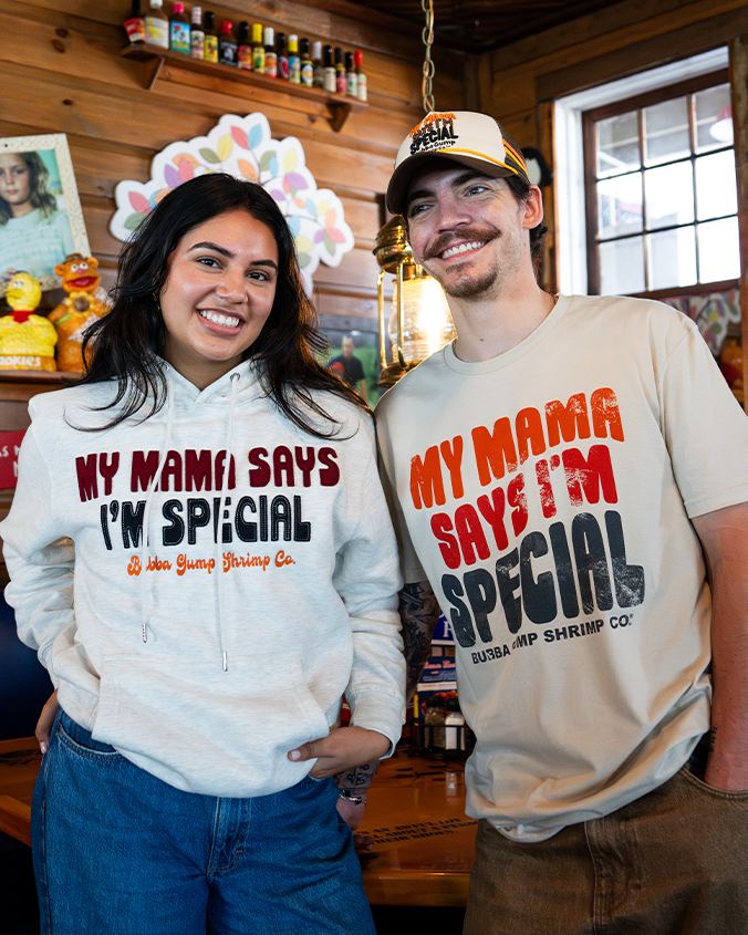 Two individuals stand side by side in a rustic setting, wearing matching tees with "MY MAMA SAYS I'M SPECIAL" text.