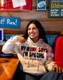 A person wearing a white hoodie with the text "MY MAMA SAYS I'M SPECIAL" sits relaxed at a wooden table in a cozy restaurant.
