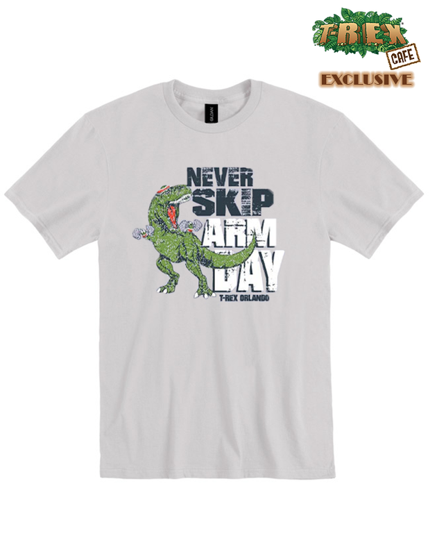 A grey T-shirt featuring a humorous graphic of a muscular green T-Rex with the text ‘NEVER SKIP ARM DAY’ and highlighting the iconic short arms of the dinosaur in a playful manner. Top right corner of image shows ‘T-REX ORLANDO - T-REX CAFE EXCLUSIVE’ logo below, 