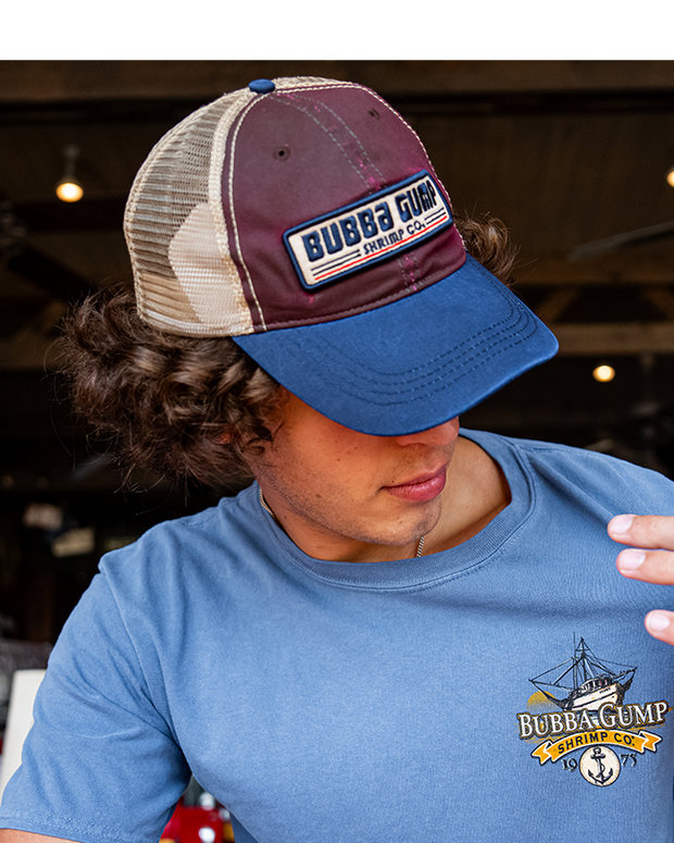 close up of male model wearing Brown cap with retro Bubba Gump logo and deep blue visor, as well as a light brown mesh back.