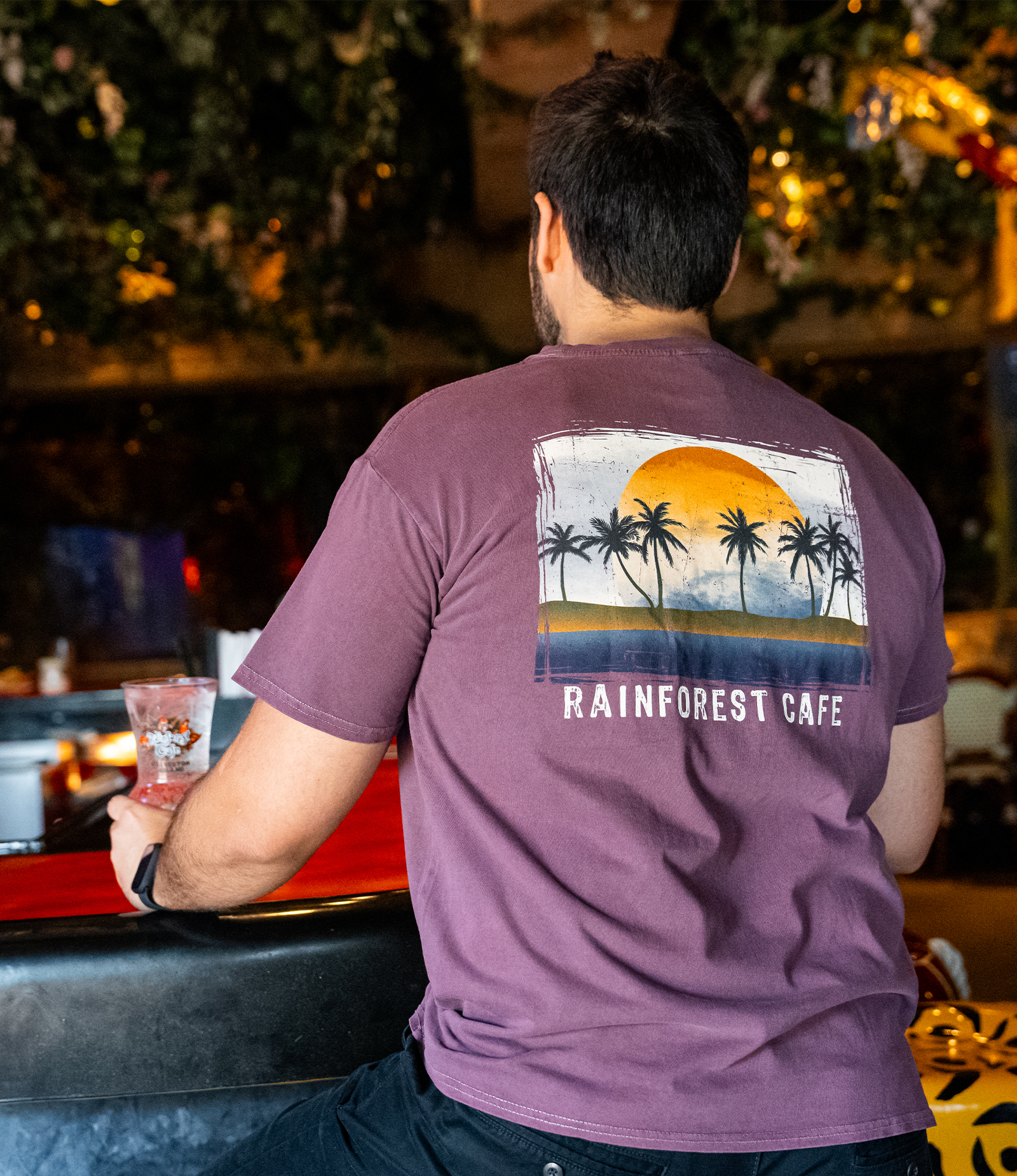 back view of male model standing at rainforest cafe bar. He is wearing our Rainforest Cafe Palm Trees Tee.