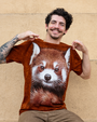 A person displays a brown t-shirt featuring a detailed print of a red panda's face against a textured beige background.