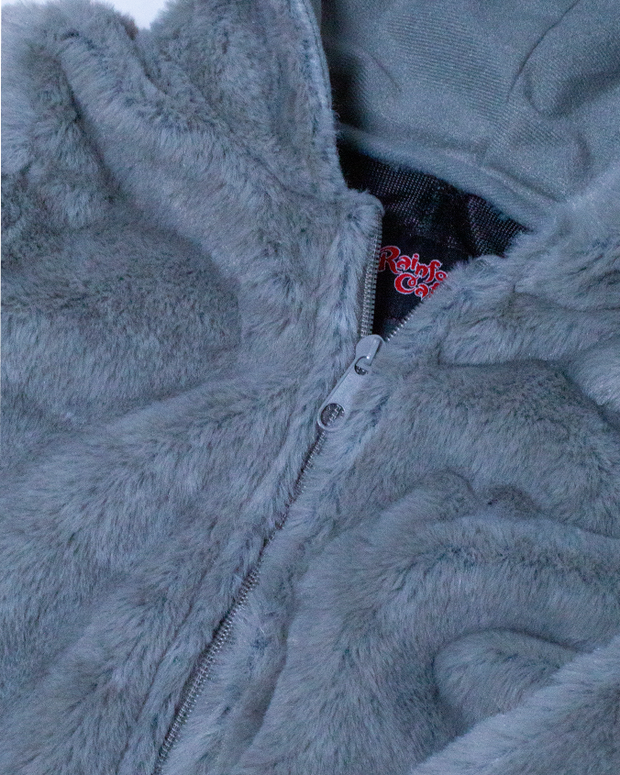 A close-up view of a grey, fluffy jacket with a partially open zipper, revealing an inner tag with red text, set against a nondescript background.