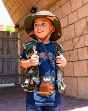 boy model in front of stone walls wearing camo vest, hat and Navy cotton shirt that has a cartoon mohawk gorilla head and Rainforest Cafe branding in orange.