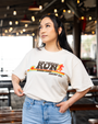 A person in a casual oversized cream t-shirt featuring "RUN FORREST RUN" and a colorful graphic stands in a lively restaurant setting.