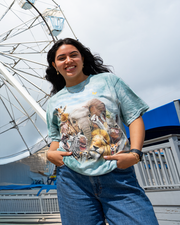 A person stands in front of a ferris wheel, wearing a light blue shirt featuring a collage of various wild animals.