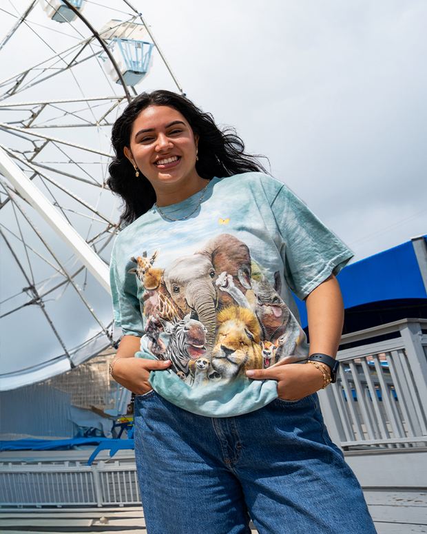 A person stands in front of a ferris wheel, wearing a light blue shirt featuring a collage of various wild animals.