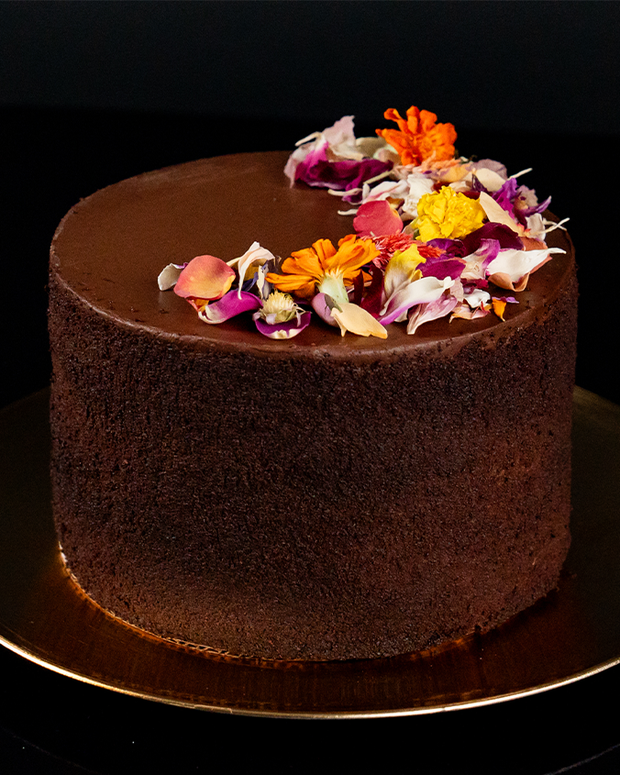 Strip House Chocolate cake topped with purple, yellow and orange flowers on 3/4 on top.