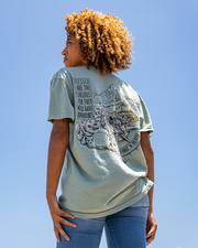 back view of female model wearing the snow leopard tee. snow leopard walking through town near mountains
