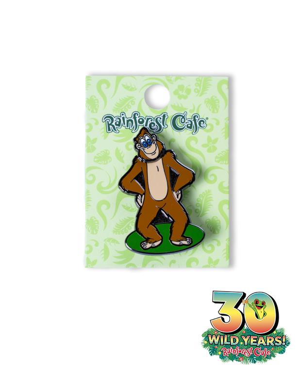 A collectible pin from Rainforest Cafe featuring a cartoon orangutan, attached to a decorative card that celebrates the cafe’s 30 wild years anniversary. The pin displays a cheerful orangutan with brown fur, hands on hips, and a wide smile. The card is adorned with green swirls on a lighter green background, with ‘Rainforest Cafe’ written in blue at the top and an emblem at the bottom right corner marking ‘30 WILD YEARS!’ with a tree frog coming out the zero.