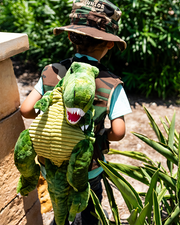 little boy walking in bushes wearing t-rex backpack