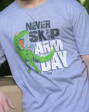 close up of grey t-shirt with a graphic of a green dinosaur and the text ‘NEVER SKIP ARM DAY’ printed on it, standing outdoors.