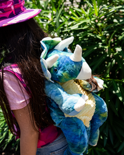 little girl standing in front of greenery wearing the triceratops backpack.
