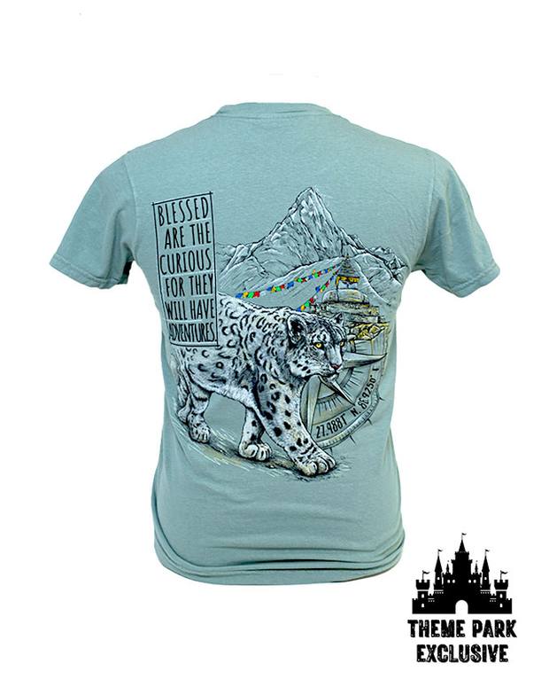 Back of tee with design of snow leopard walking through town near mountains with black  "Theme Park Exclusive" tags in corner.'