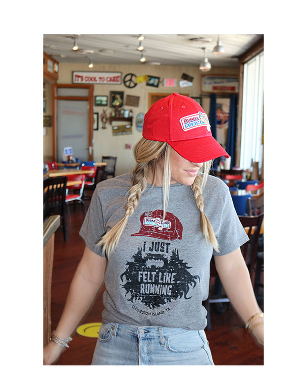 Model wearing Bubba Gump red hat  with traditional logo, wearing "I just felt like running,"Tee, Pictured inside of Bubba Gump Location. Authentic cap has adjustable, snap back closure