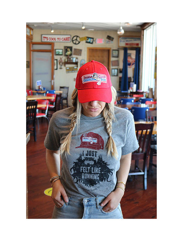 Model wearing Bubba Gump red hat with traditional logo, wearing "I just felt like running,"Tee, Pictured inside of Bubba Gump Location. adjustable, snap back closure, Authentic Cap has adjustable, snap back closure