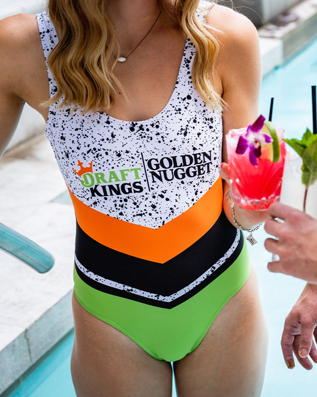 Blonde model wearing one piece swimsuit by the poolside with black splatter patterns and orange, green, and black stripes below Draft Kings/Golden Nugget logos.