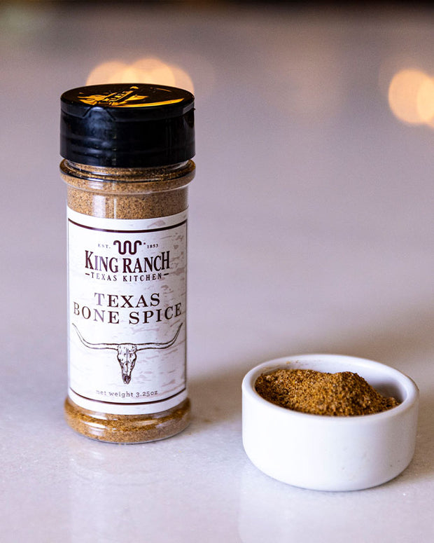 King Ranch Texas Bone Spice with small bowl of spice sitting on white table with background blurred out.