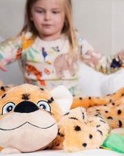 Little girl standing behind Maya the Jaguar plush blanket that is laying on bed.