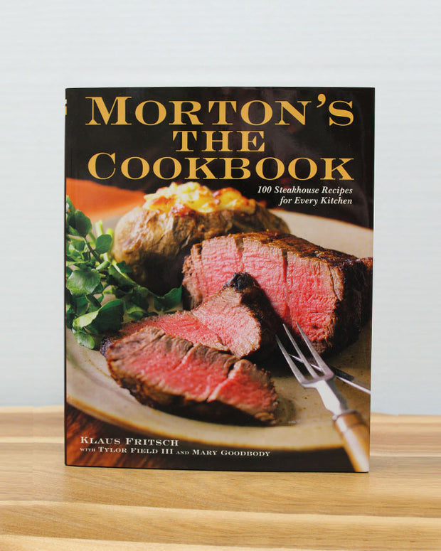 Morton's The Cookbook on light brown wood in front of white background.