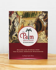 The Palm Restauraunt Cookbook on light brown wood in front of white background.