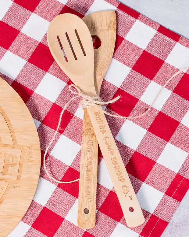 Red, white checkered towel layered under bamboo spoon & spatula.  Spoon & Spatula have lasered Bubba Gump Shrimp Co. on handles.