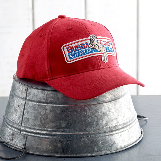 Authentic Forrest Gump cap sitting on top of upside down metal bucket in front of white panel background.