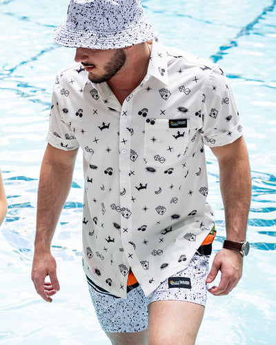 Man wearing white shirt with black icons by the poolside.