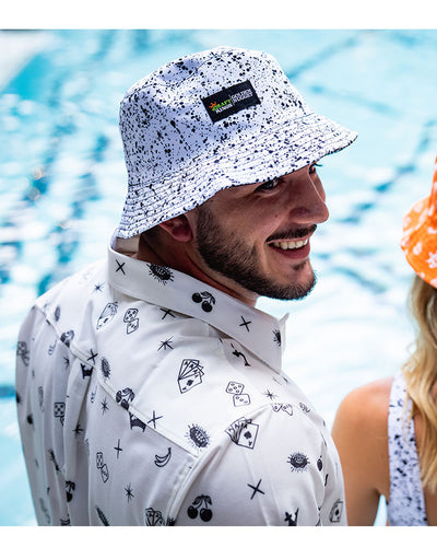 Man wearing black and white Splatter Bucket Hat and White Icon Tee while standing on the poolside.