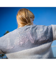 Blonde woman wearing Radiate Love jersey and posing to show the back in front of a blue sky background.